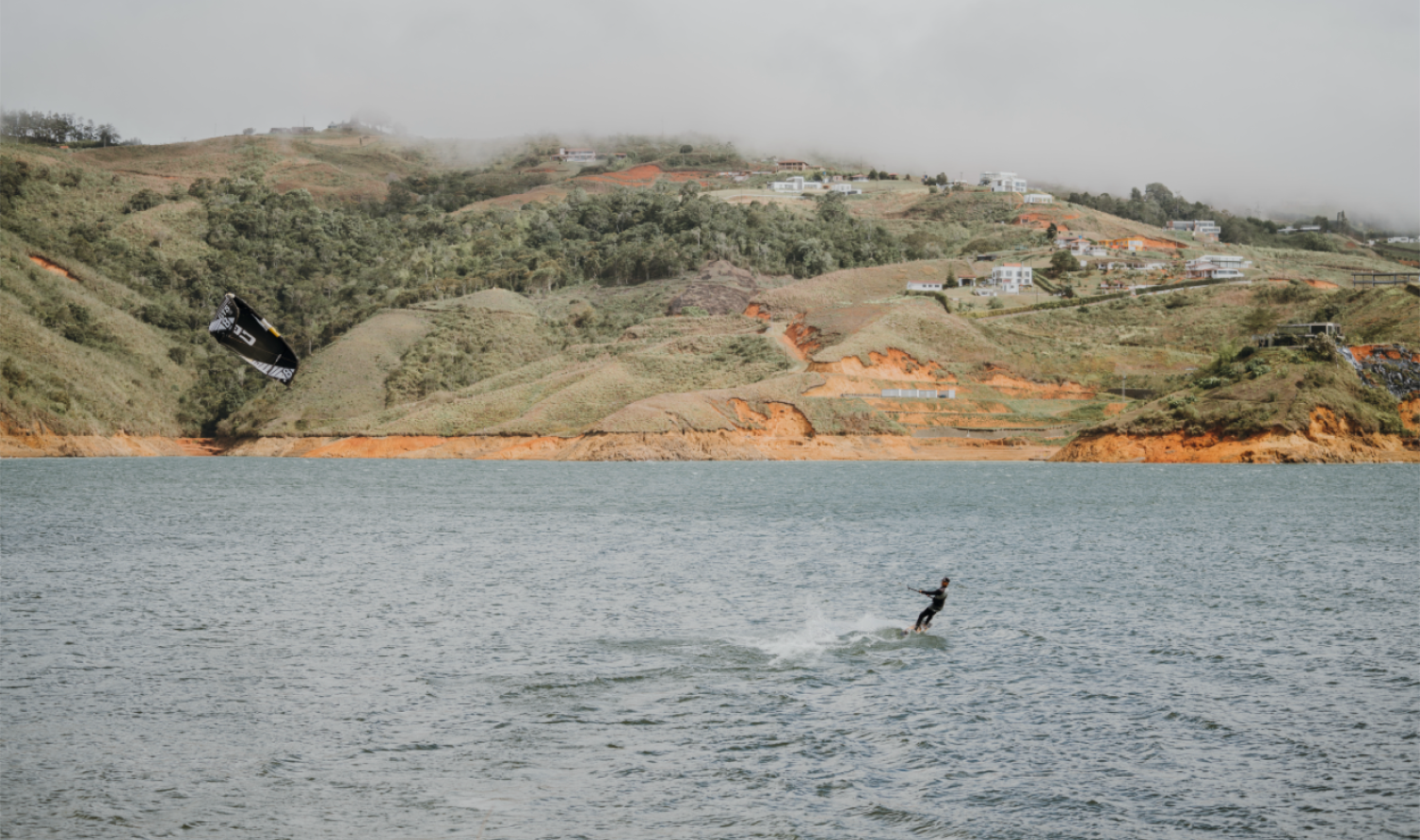 A kite-surfer gliding across the water near BJJ Camp XP, with lush hills in the background, showcasing the exciting outdoor activities available to participants at the camp.