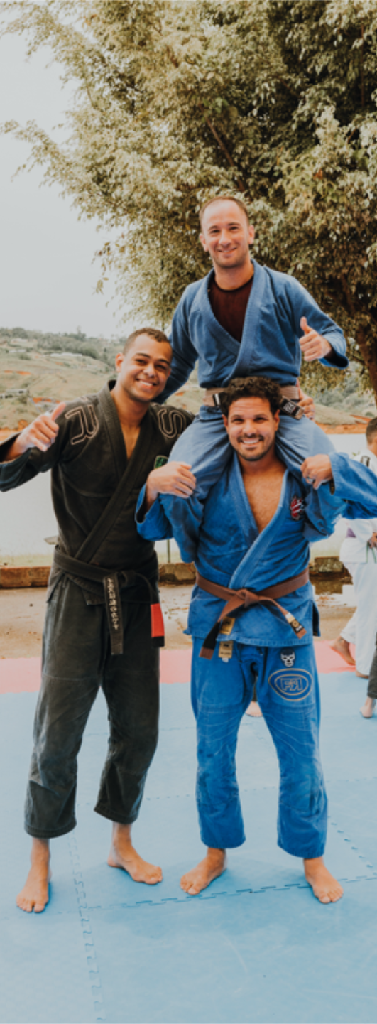 Three participants at BJJ Camp XP posing happily on the mats, with one on another's shoulders, celebrating the camaraderie and friendships formed during their Jiu-Jitsu training.