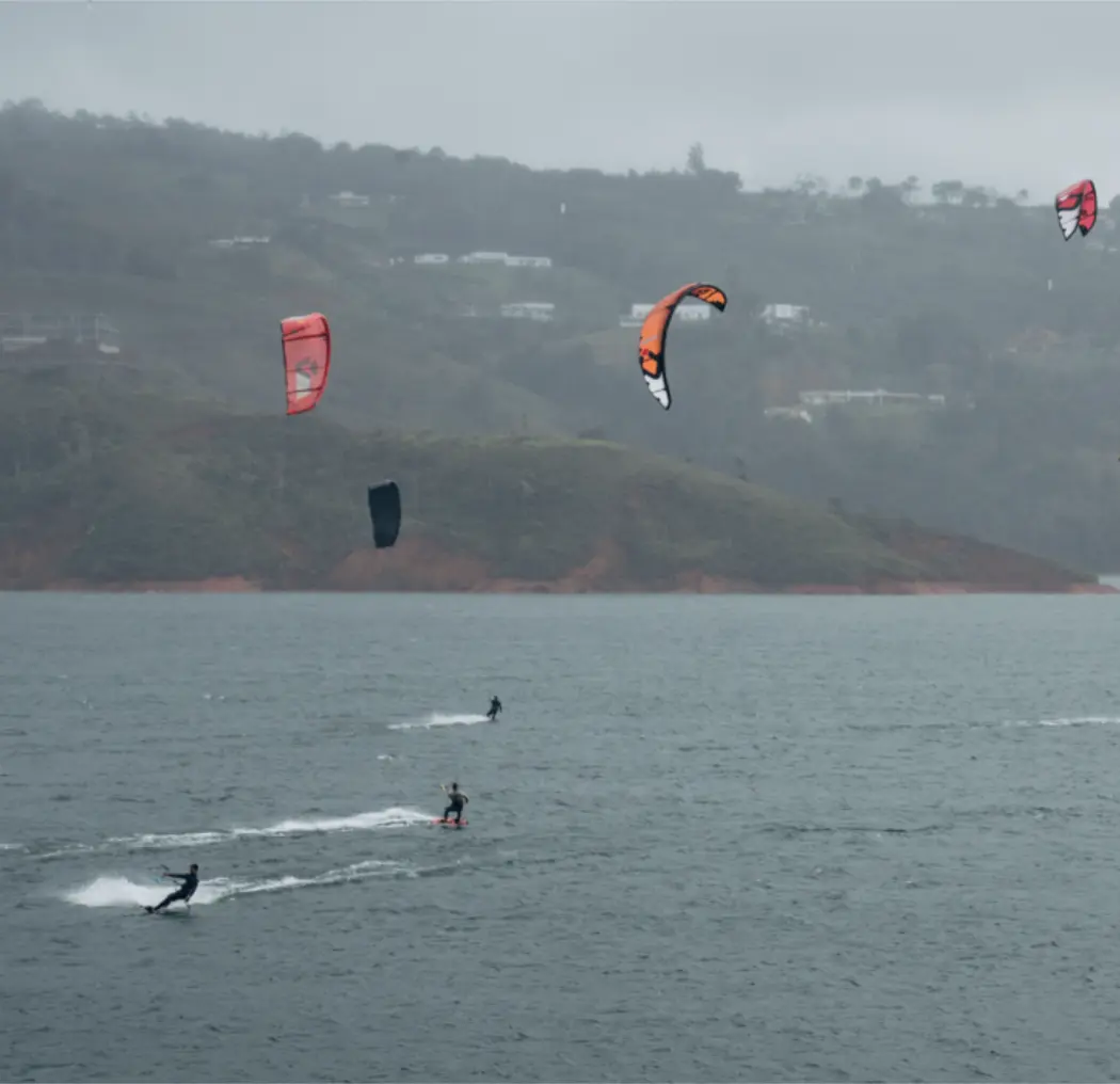 Kite-surfers enjoying the waters of Calima, Colombia, with colorful kites in the sky and lush hills in the background, highlighting the adventurous spirit of BJJ Camp XP.