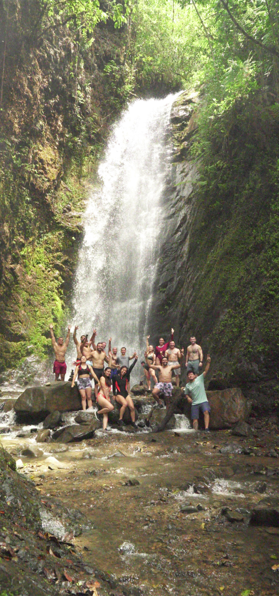 Group of BJJ Camp XP participants posing joyfully at a waterfall, showcasing the fun and camaraderie experienced during their time at the camp amidst nature's beauty.