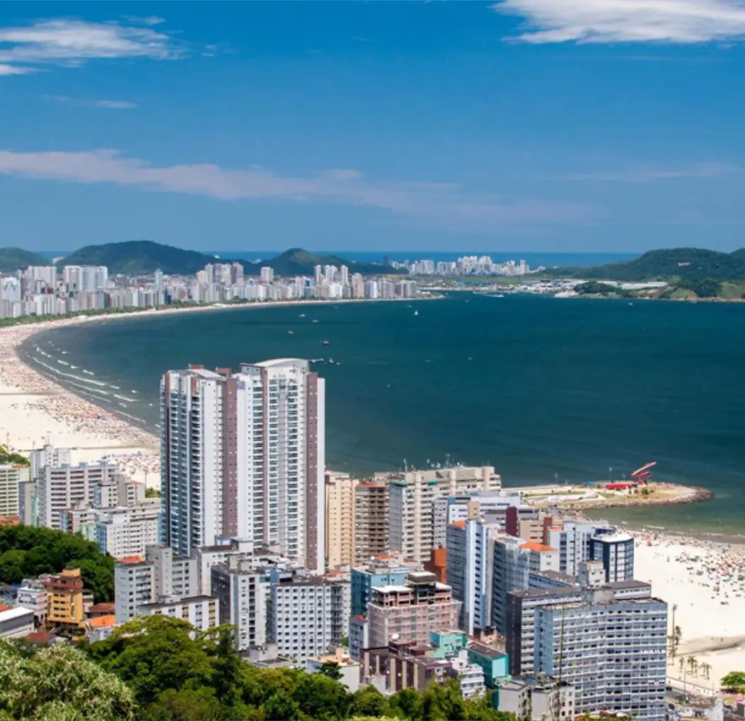 Aerial view of Santos, Brazil, featuring the coastline with its sandy beach, modern high-rises, and the lush hills in the background, highlighting the beauty of the city.