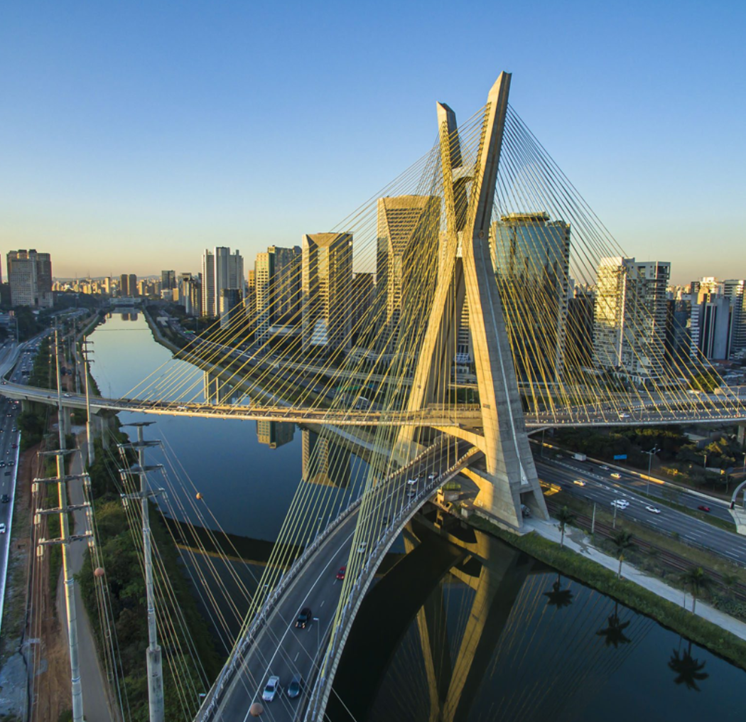 Aerial view of the Estaiada Bridge in São Paulo, Brazil, showcasing its unique design, surrounding skyscrapers, and the serene reflection on the water.