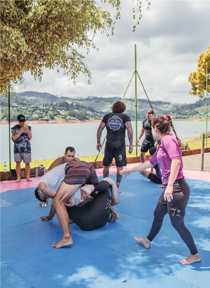 Group of Jiu-Jitsu practitioners training outdoors at a BJJ camp in South America, near a scenic lake and mountains.