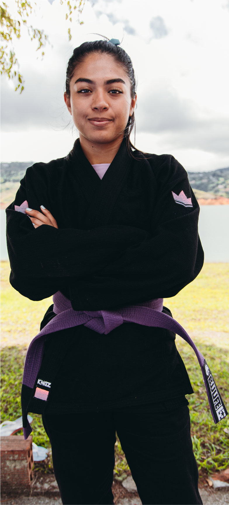 Camila, a participant in the XP Athlete Program, wearing a black gi with a purple belt, standing confidently outdoors.