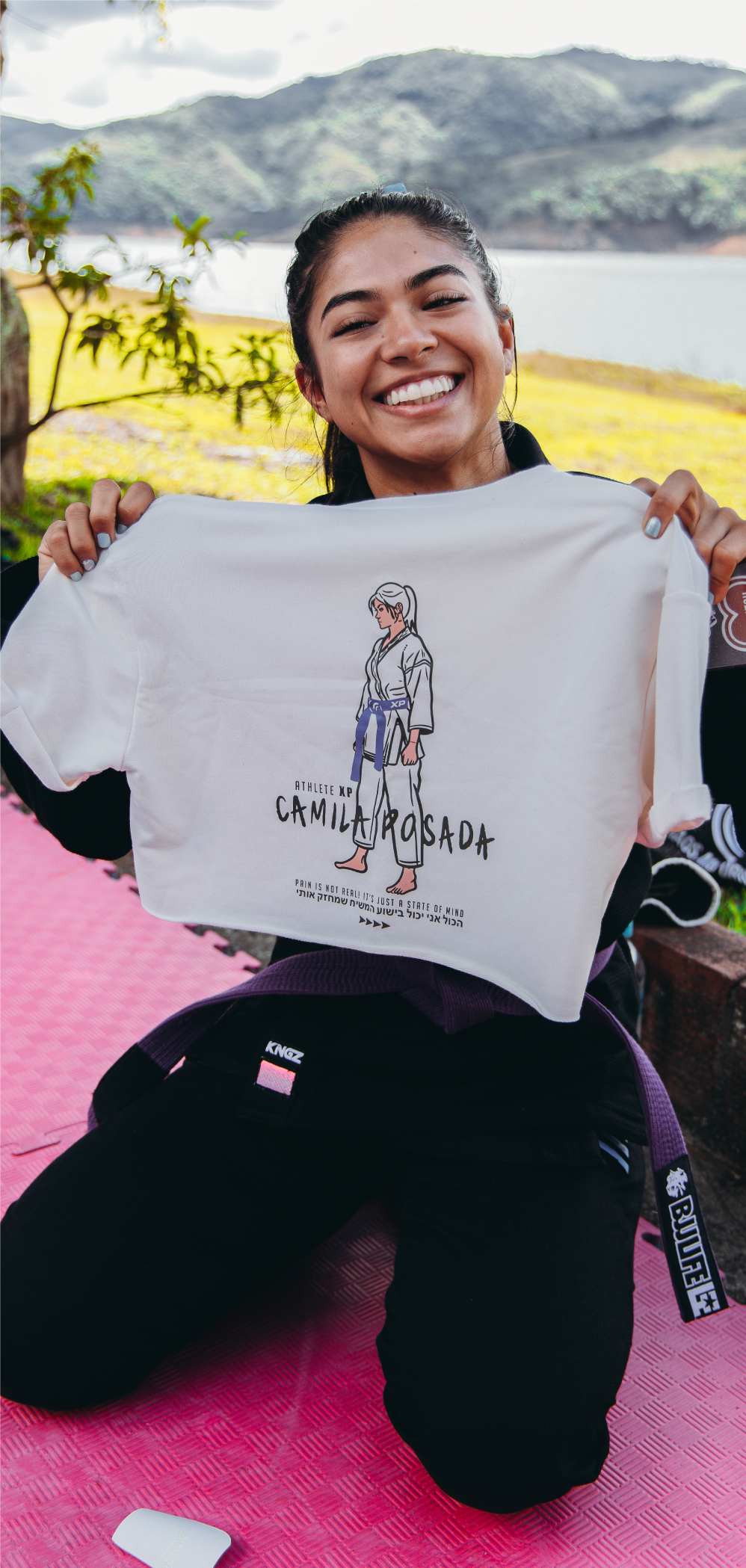 Camila, XP Athlete Program participant, smiling and holding a custom T-shirt featuring her illustration in a Jiu-Jitsu gi.