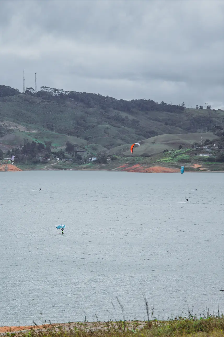 Kitesurfers gliding on Lake Calima, a popular activity offered at BJJ Camps for Backpackers in South America, surrounded by green hills.