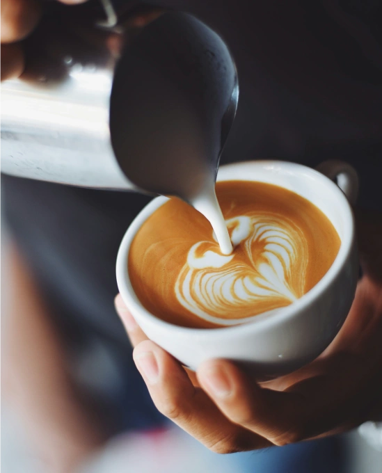 A close-up of a barista pouring latte art into a coffee cup, highlighting Colombia’s coffee culture for backpackers after BJJ Camp.