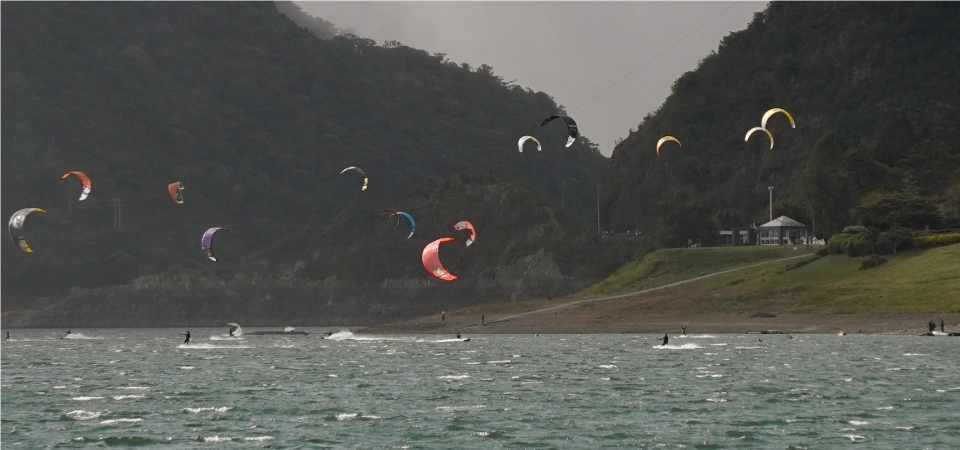 Kitesurfers on a scenic lake surrounded by mountains, blending watersports and BJJ training while traveling.