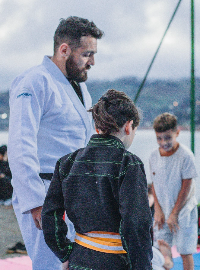 Leonidas Benjumea in a white gi guiding young Jiu-Jitsu practitioners during an outdoor session by a scenic lake in Colombia.