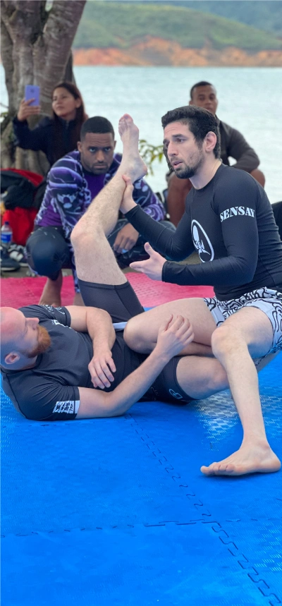 Alex Ecklin demonstrating BJJ techniques with a student on a blue and red mat at the Alex Ecklin BJJ Camp in Calima, Colombia.