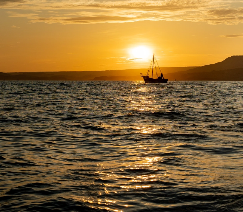 Sunset over the Pacific Ocean in Peru with fishing boat silhouette, part of a Brazilian Jiu Jitsu Camp in Peru experience.