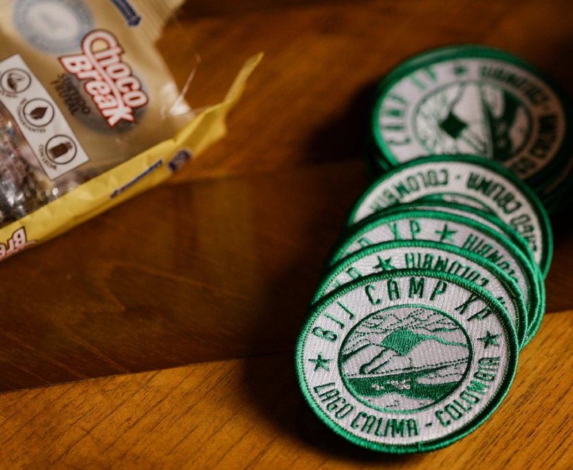 XP Camp patches on wooden table representing community at a Brazilian Jiu Jitsu Camp in Peru.